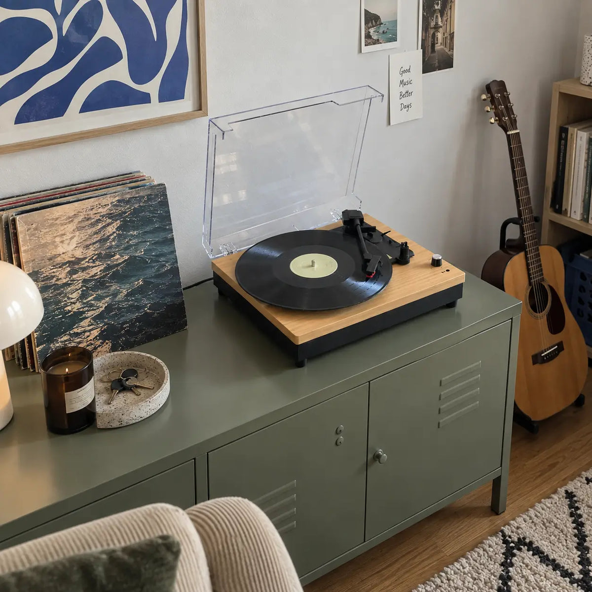 Record player on a green cabinet beside a guitar and a stack of records