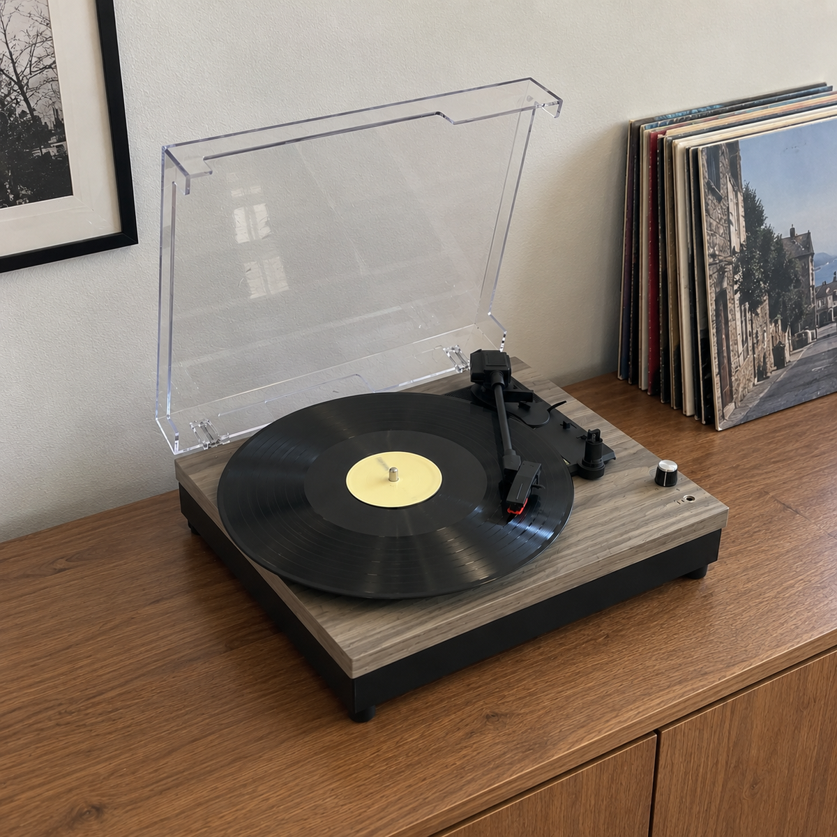 Record player with a clear lid on a wooden sideboard, next to a row of records